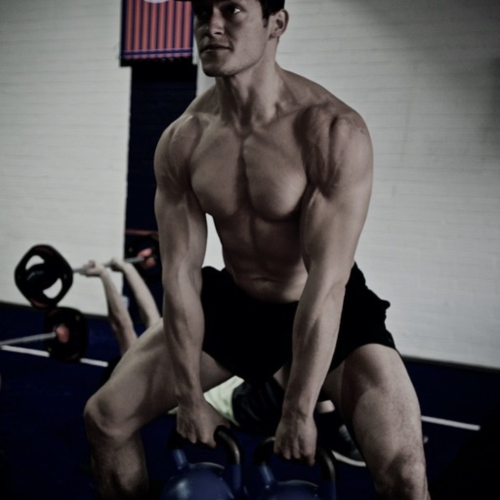 Andreas Soler en acción concentrado realizando una rutina de ejercicios deltoides con pesas rusas, simbolizando la fuerza y la dedicación requeridas en el fitness avanzado.