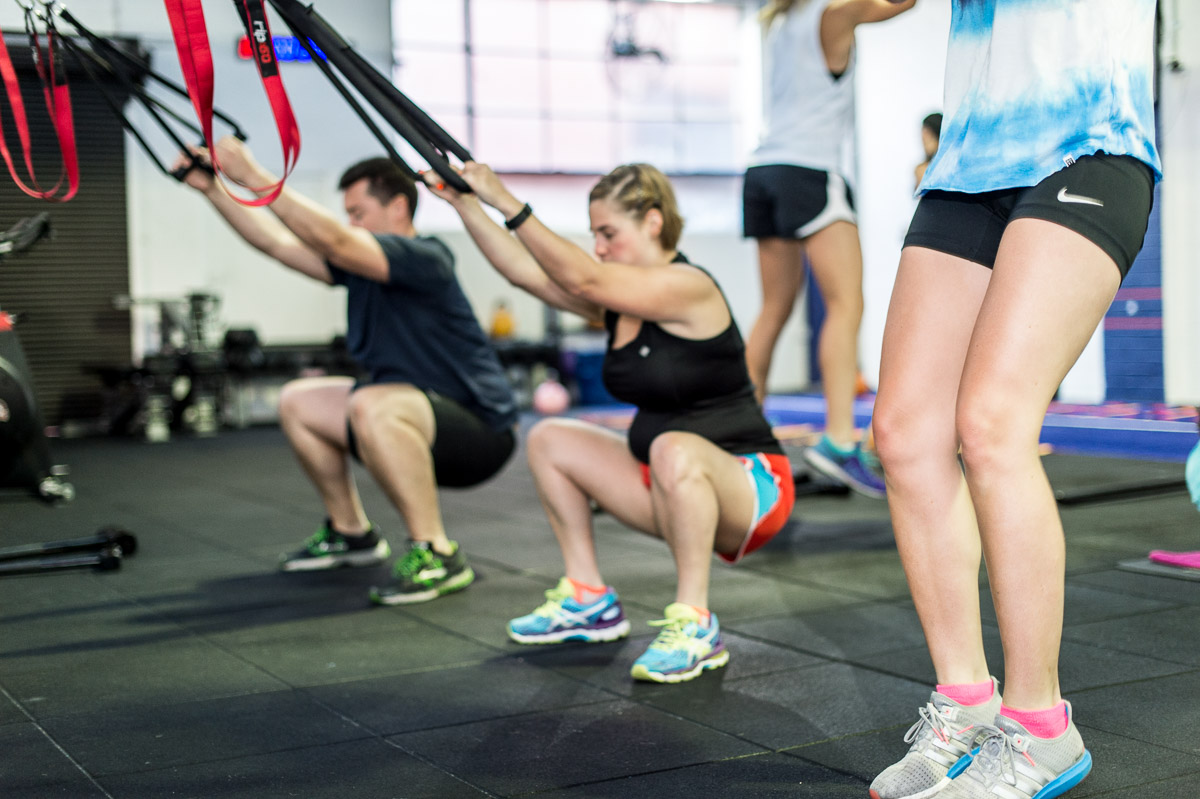 Personas en plena rutina de ejercicios para piernas utilizando bandas de suspensión TRX en el gimnasio